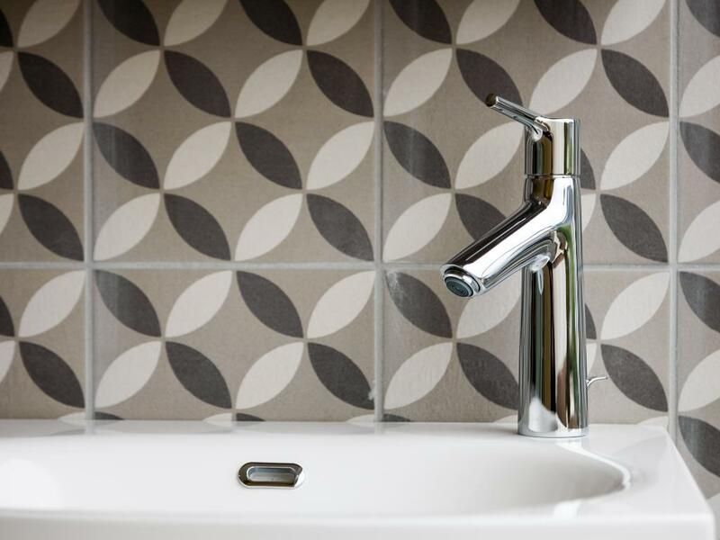 Robinet de salle de bain chromé moderne au-dessus d'un lavabo blanc avec crédence en carrelage géométrique.