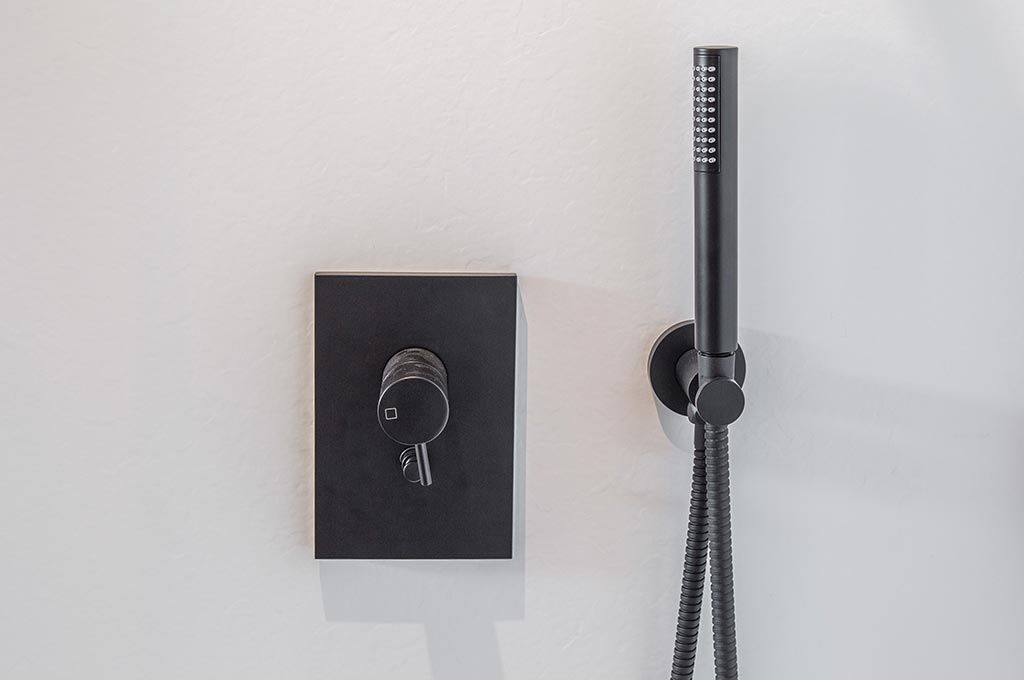 Panneau de commande de douche noir et pommeau de douche à main fixés sur un mur blanc de salle de bain.