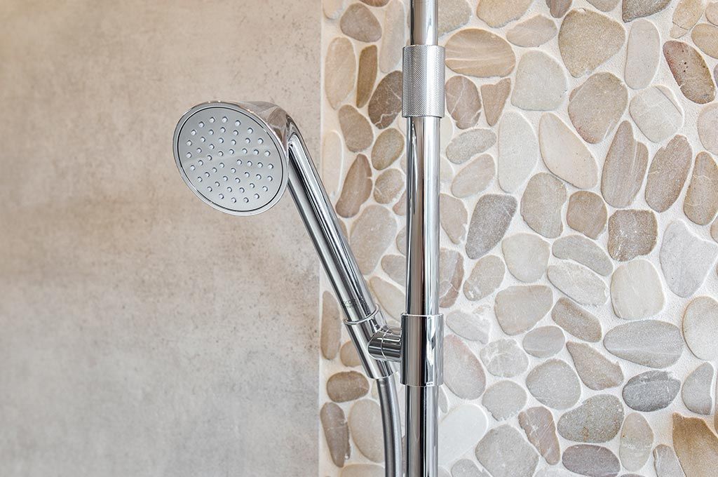 Pommeau de douche sur un tuyau de douche argenté contre un mur de salle de bain carrelé en pierre