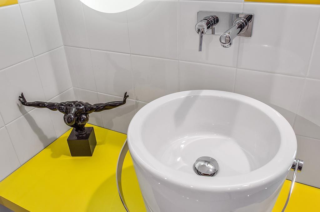 Lavabo de salle de bain blanc avec robinet chromé et sculpture de tête de taureau noire sur un comptoir jaune vif.