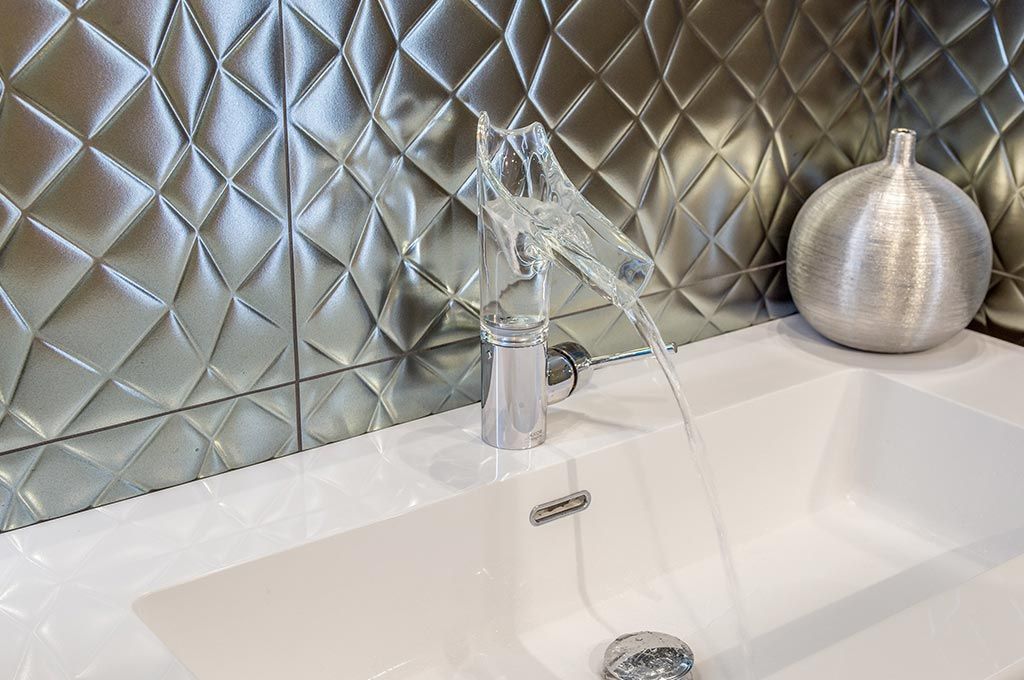 Robinet de salle de bain chromé déversant de l'eau dans un lavabo blanc avec une crédence matelassée métallique et un vase décoratif argenté