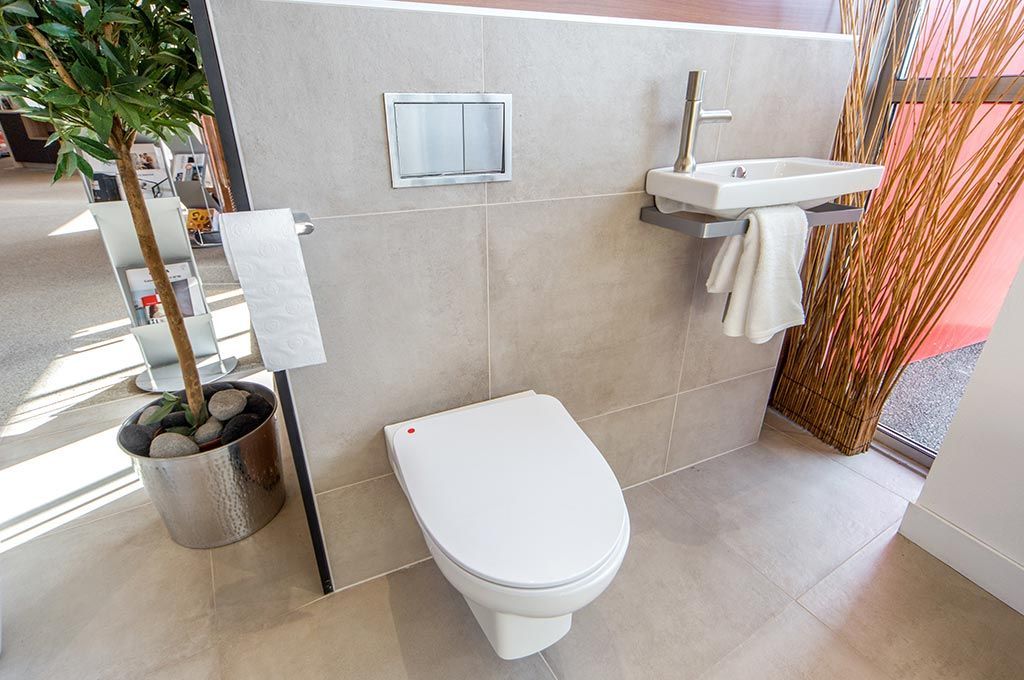 Salle de bains moderne avec toilettes blanches, lavabo mural et carrelage beige.