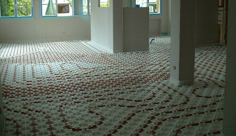 Pièce vide, moquettée, avec un sol à motifs et de grandes fenêtres laissant entrer la lumière du jour.