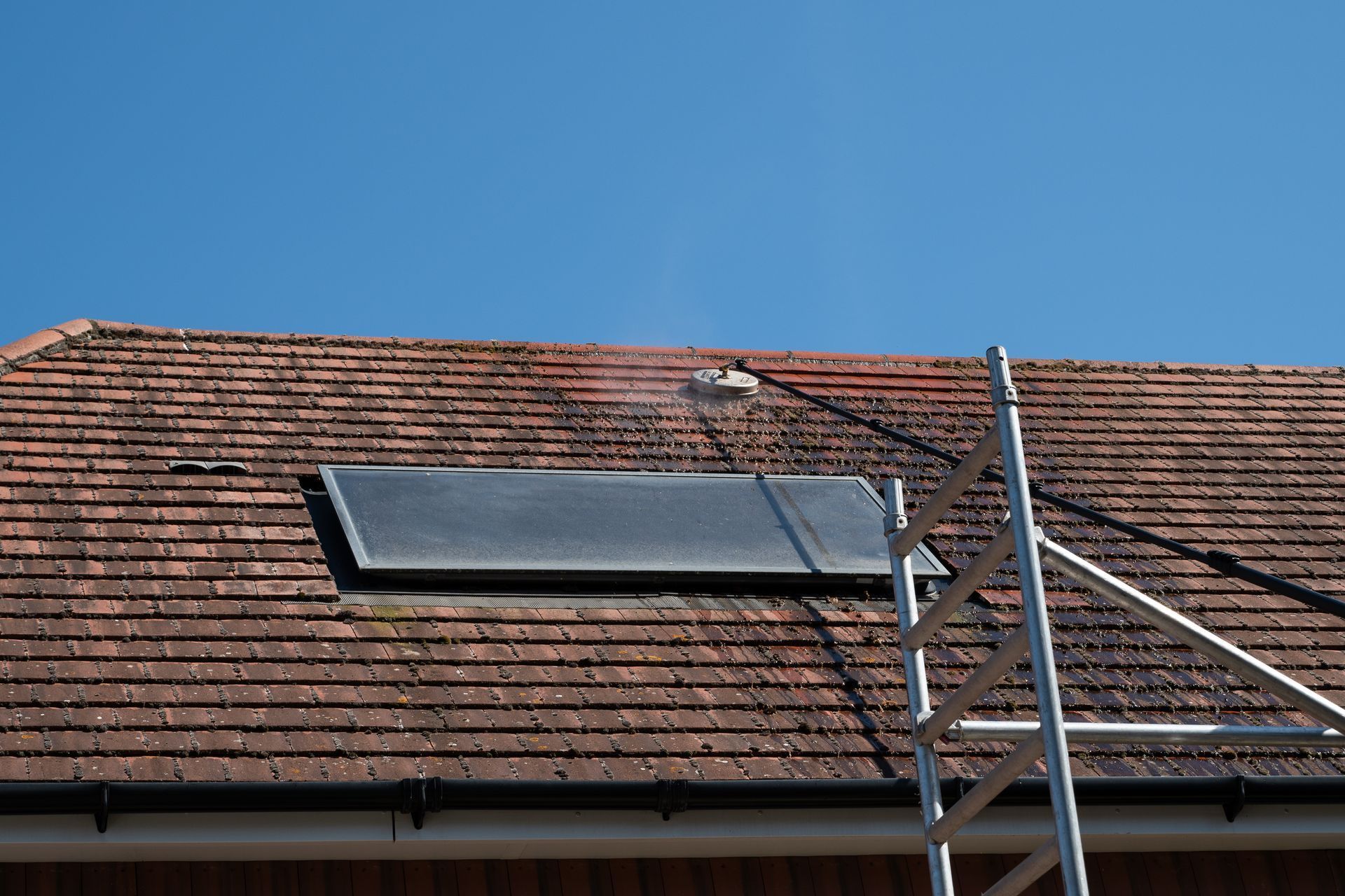 Red tiled roof being cleaned with a pressure washer; scaffolding to the side; solar panel on the roof.