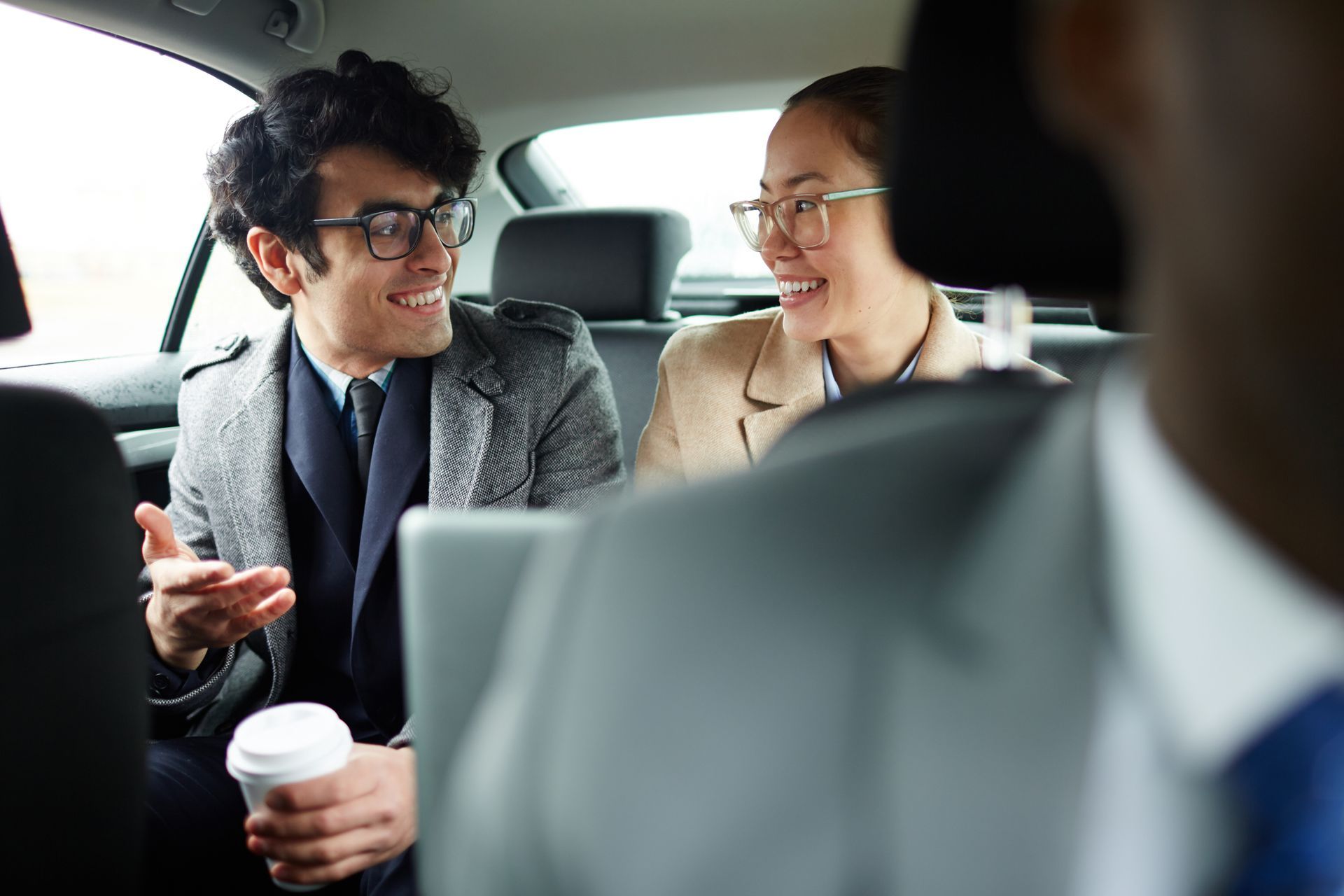 Deux collègues discutent dans une voiture, l’un tient un gobelet de café et sourit.
