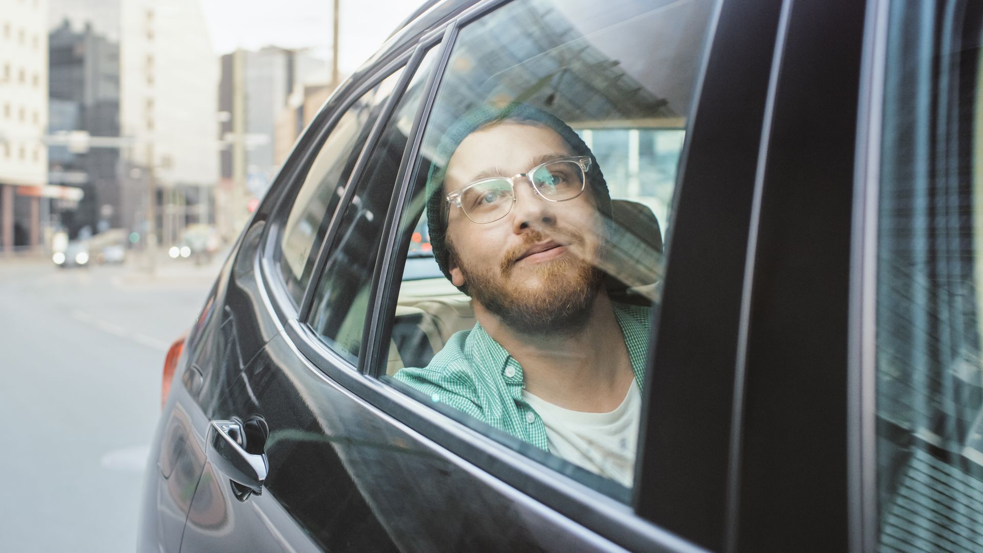 Un homme regarde par la fenêtre d’une voiture dans une rue en ville, il porte des lunettes et un tee-shirt vert