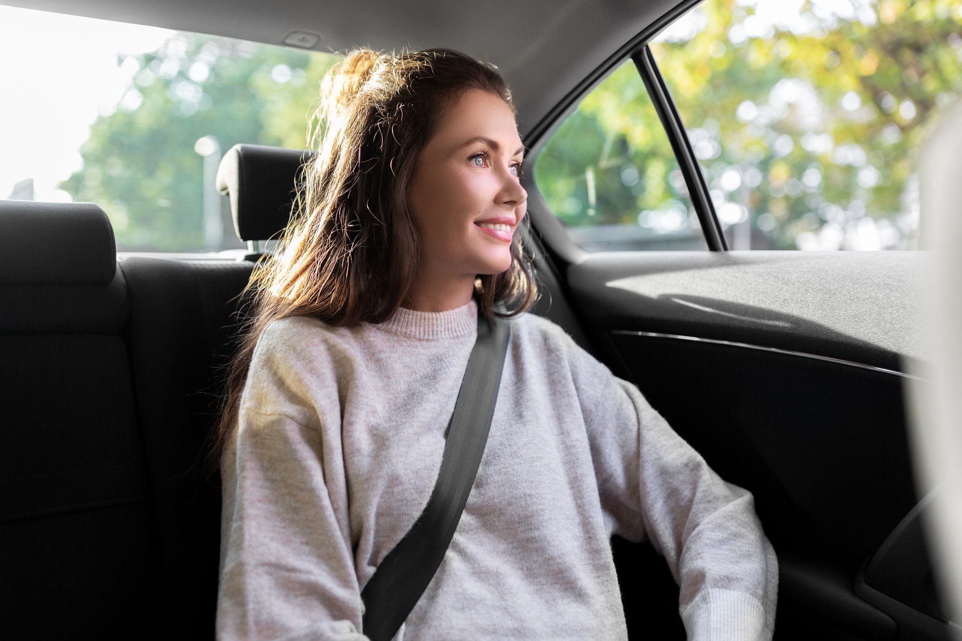 Un passager souriant sur la banquette arrière d’une voiture, portant sa ceinture de sécurité et regardant par la fenêtre