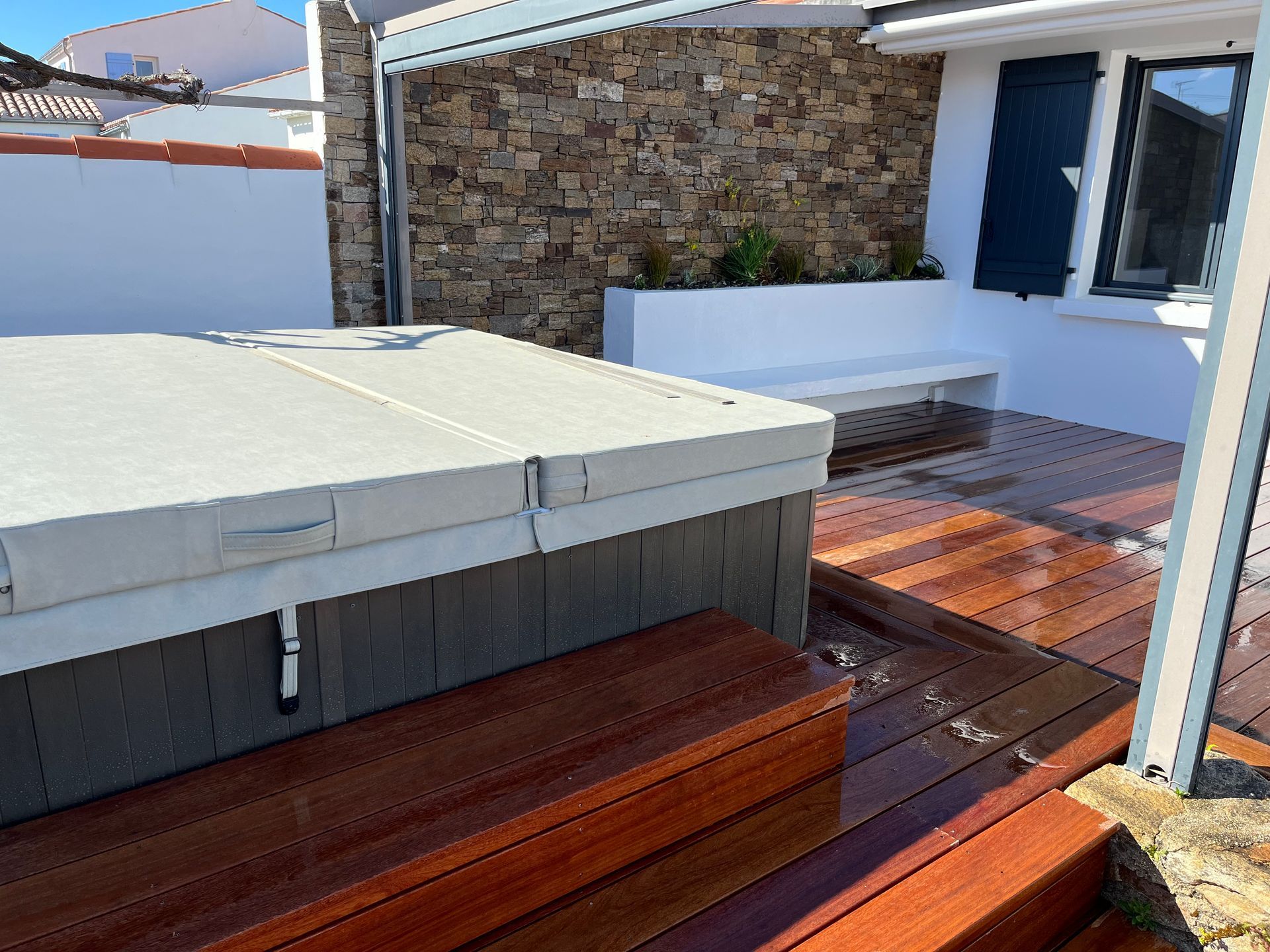 Terrasse en bois avec chaises blanches modernes, à côté d'un jardin en pierre, près d'une maison avec de grandes fenêtres.