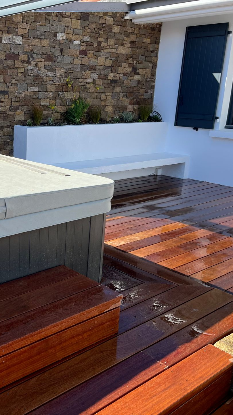 Terrasse en bois avec eau, menant à un banc blanc et un mur de pierre avec verdure.