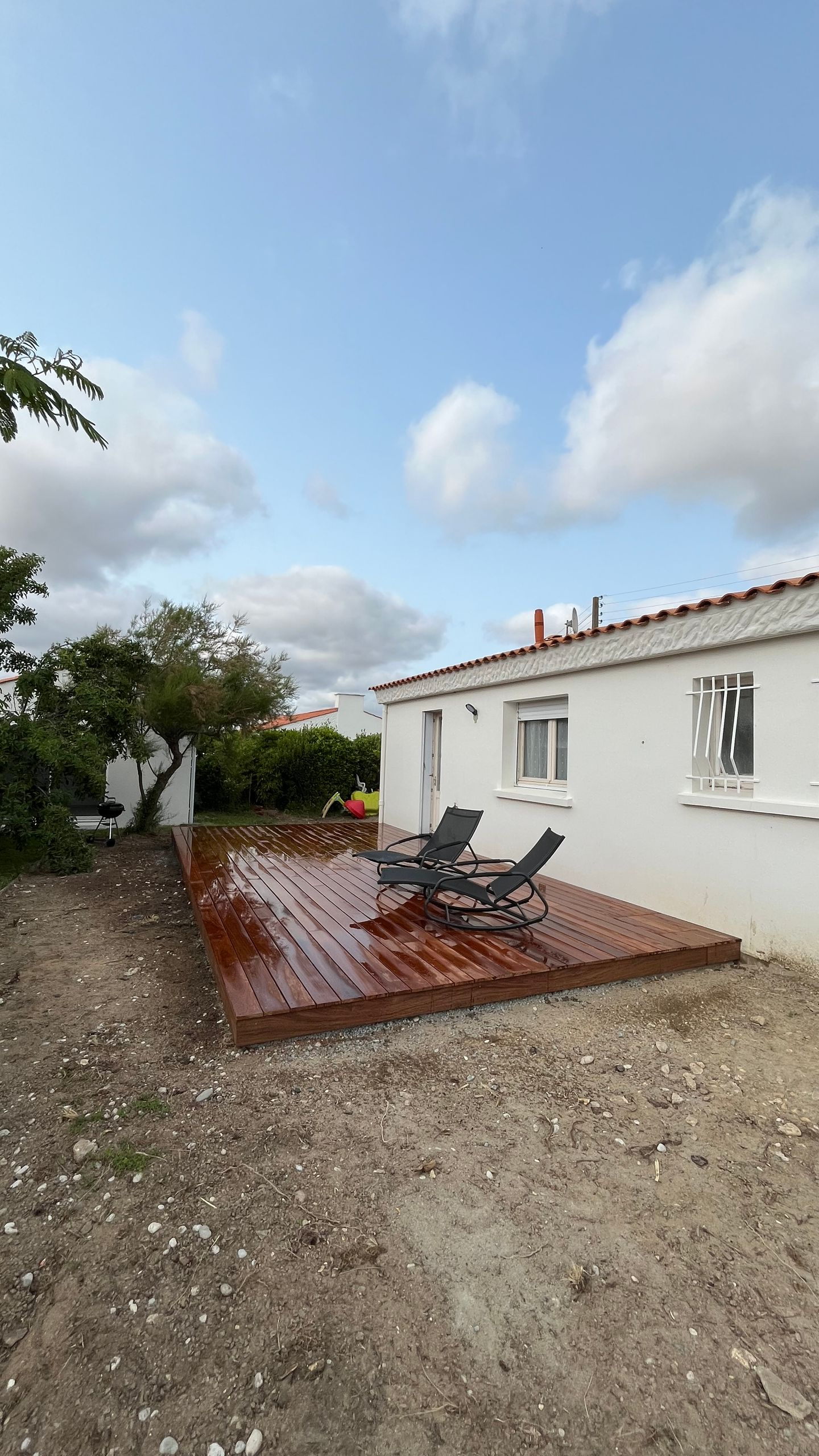 Terrasse en bois avec deux chaises à côté d'une maison blanche. Ciel nuageux au-dessus.