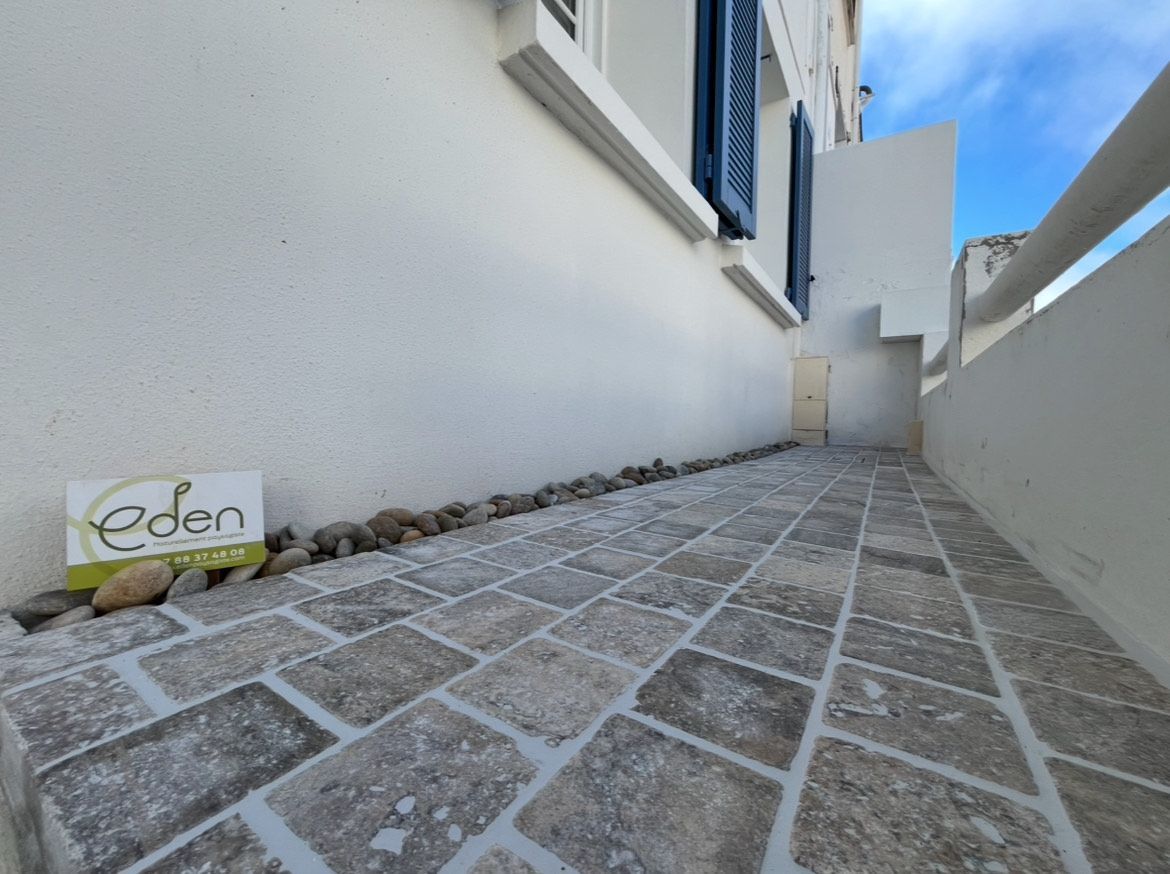 Allée courbée en pierre grise bordée d'arbustes verts et de paillis brun.