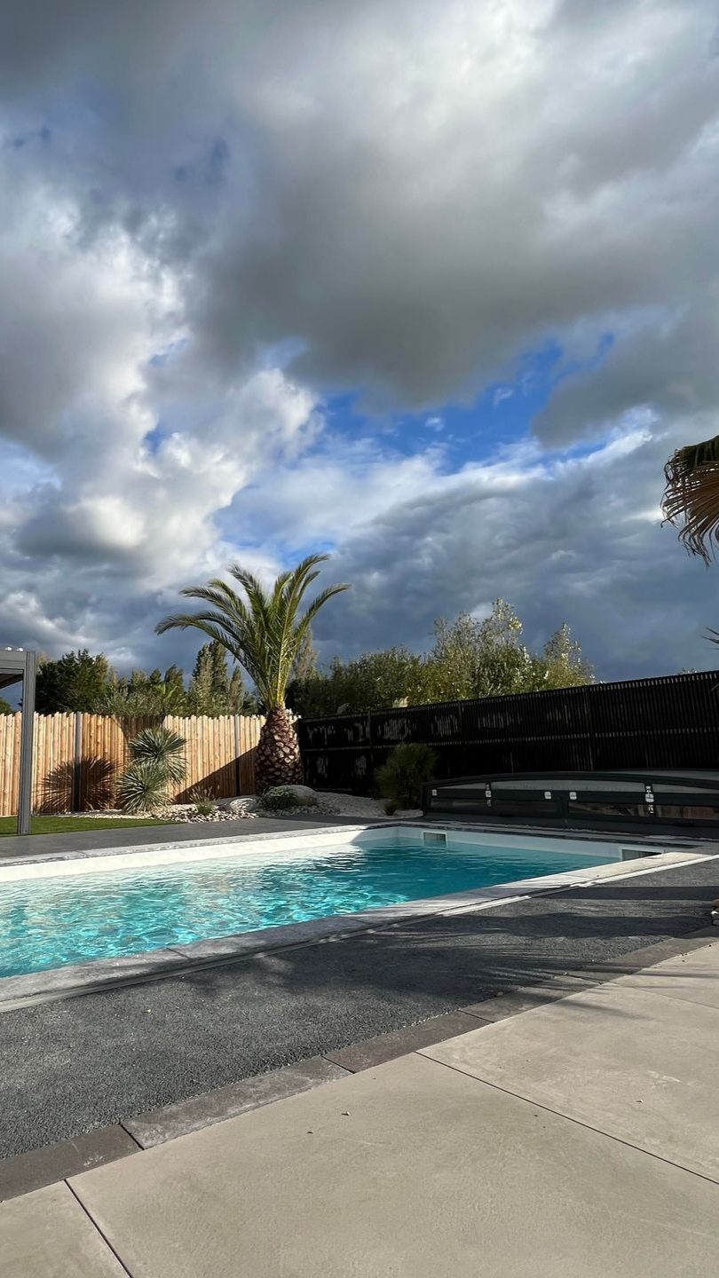 Piscine sous un ciel nuageux avec un palmier et une clôture en bois.