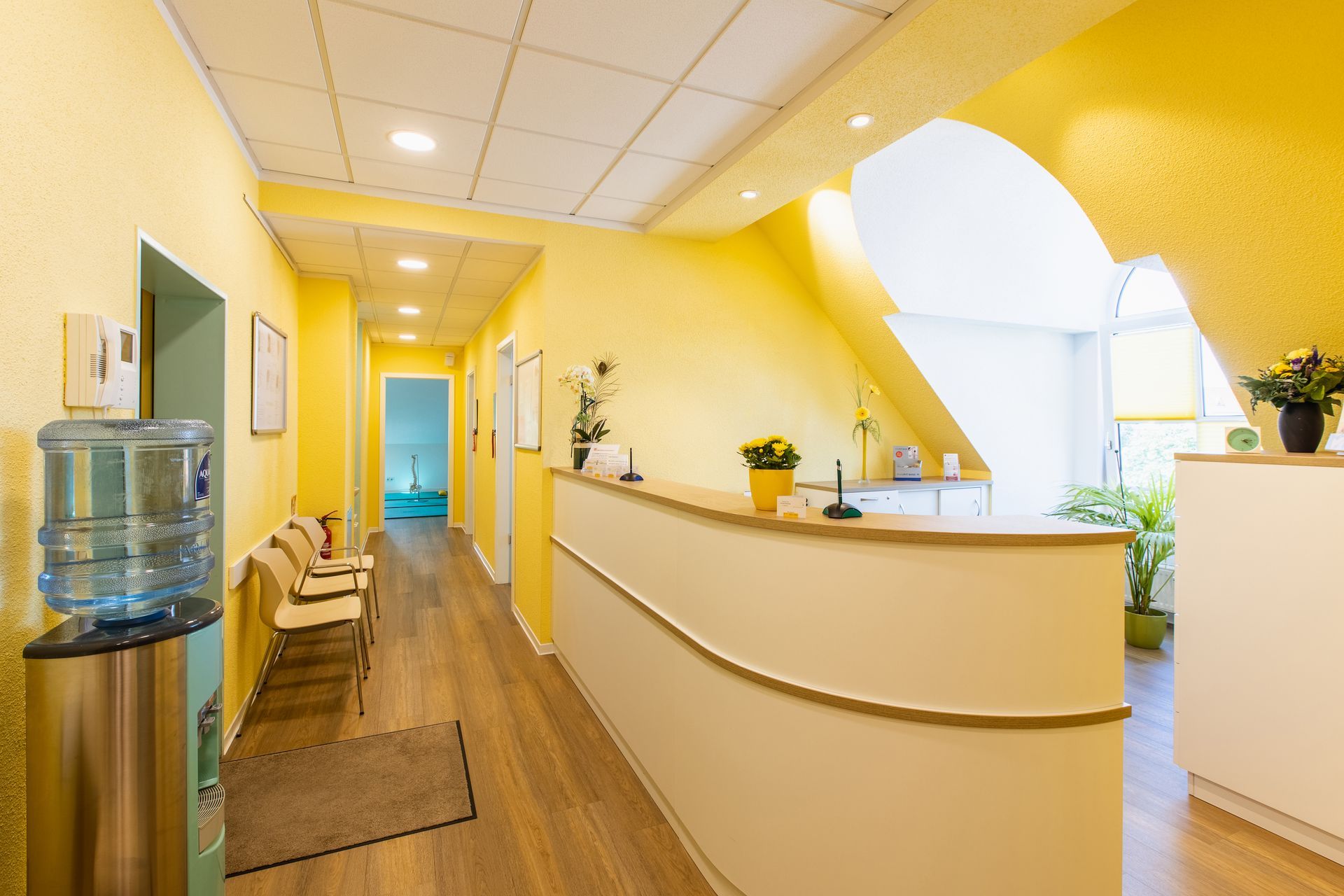 Helles, gelb gestaltetes Foyer und Empfangsbereich einer Physiotherapie-Praxis.