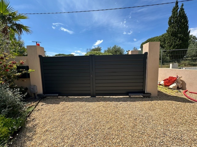 Un portail noir se trouve au milieu d'une allée de gravier.