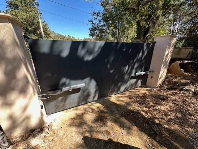 Une clôture avec un portail gris et des arbres en arrière-plan