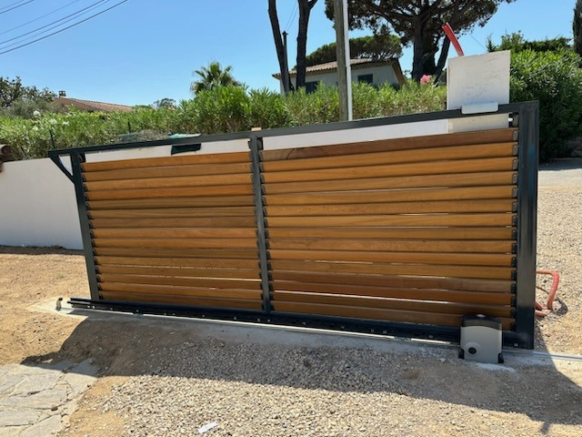 Une clôture en bois avec un portail coulissant devant une maison