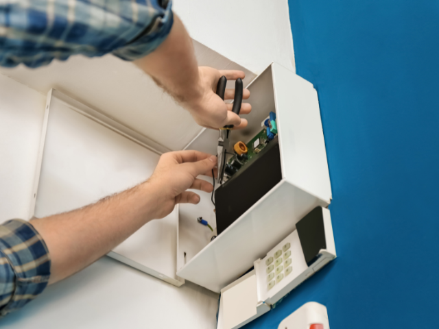 Un homme répare un système de sécurité avec un tournevis.