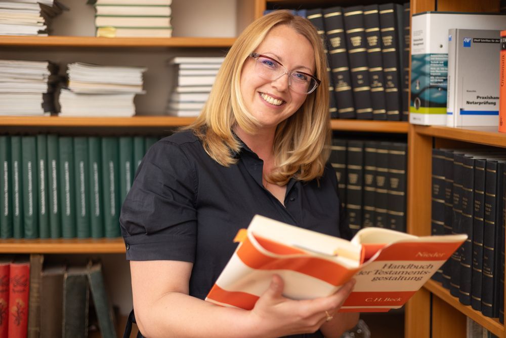 Eine Frau mit Brille sitzt an einem Schreibtisch vor einem Computer.
