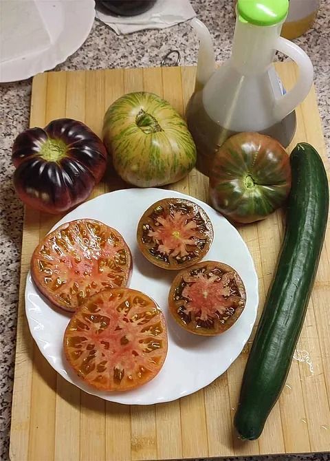 Un plato de tomates y un pepino en una tabla de cortar.