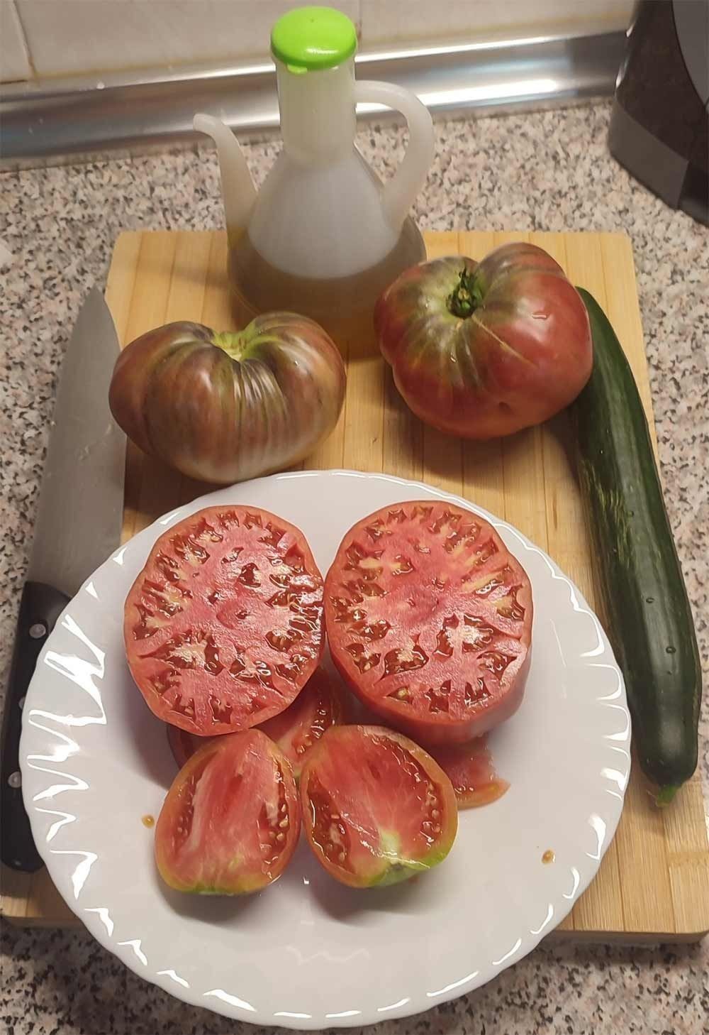 Un plato de tomates, pepinos y aceite de oliva en una tabla de cortar.