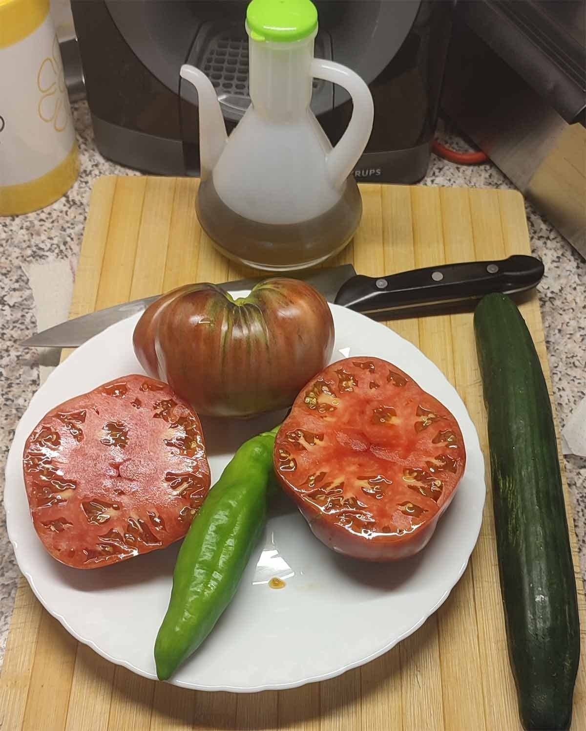 Un plato de tomates, pimientos y pepinos en una tabla de cortar.