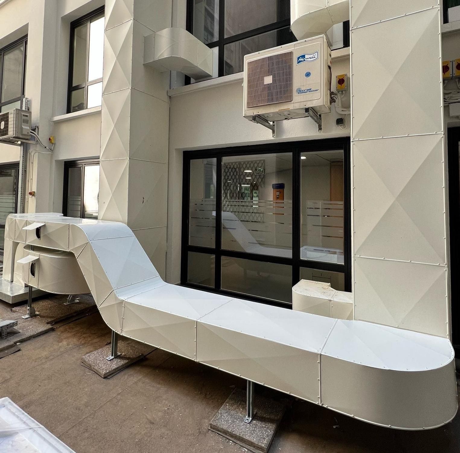 Système de conduits d'air blancs sur supports à l'extérieur d'un bâtiment avec portes vitrées.