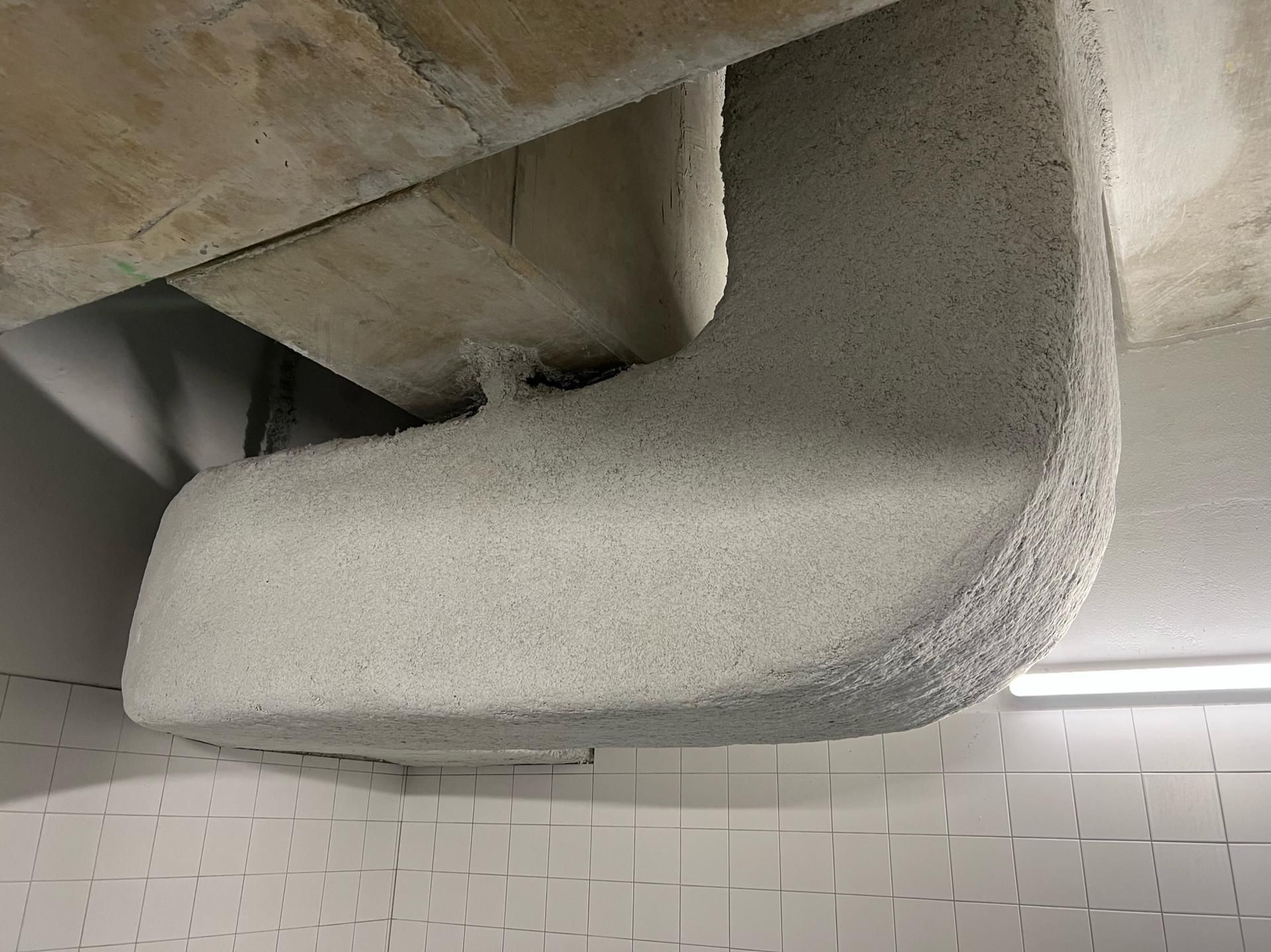 Tuyau gris, arrondi, texturé et isolé sous un plafond en béton, avec un mur carrelé blanc en dessous.