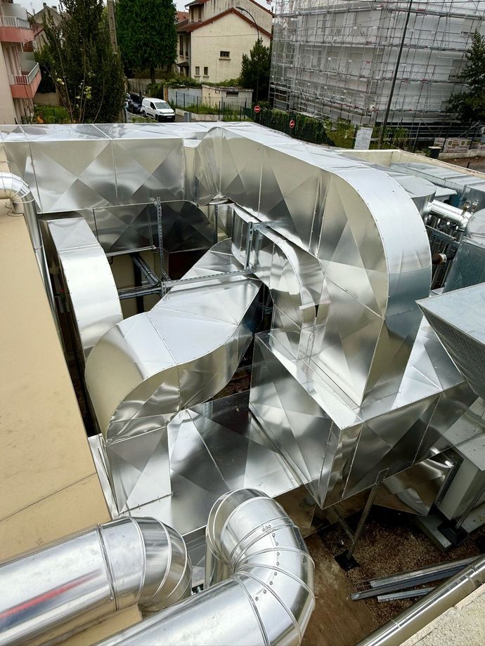 Conduits métalliques galvanisés sur le toit d'un bâtiment, avec des sections courbes et des structures environnantes.