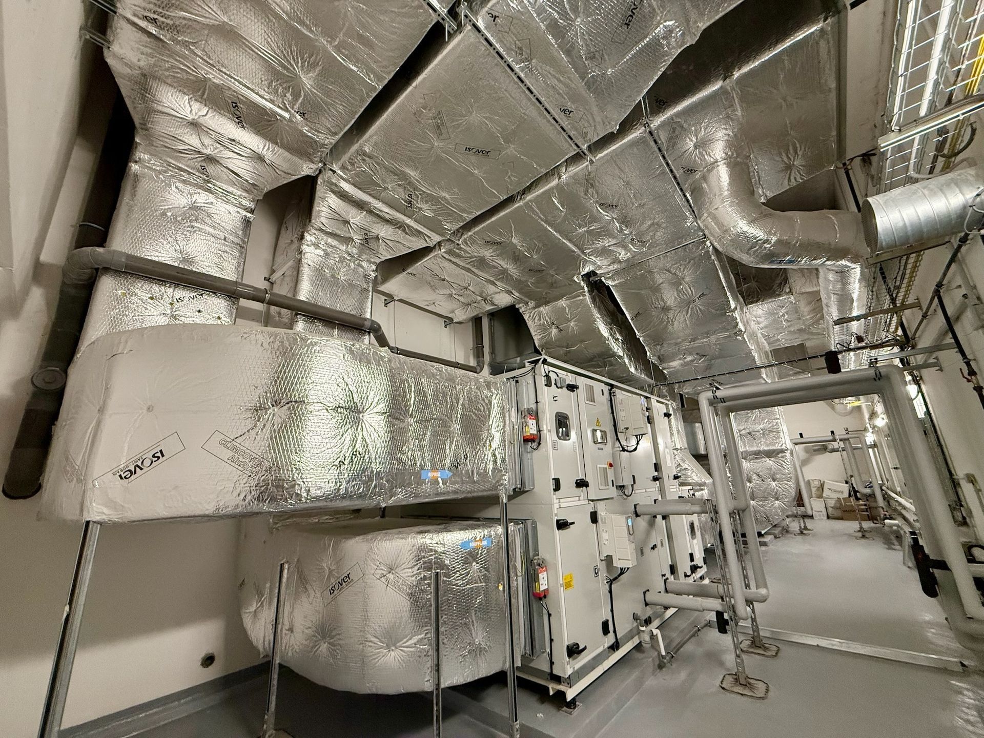 Système CVC avec conduits et équipements isolés en argent dans une salle mécanique.