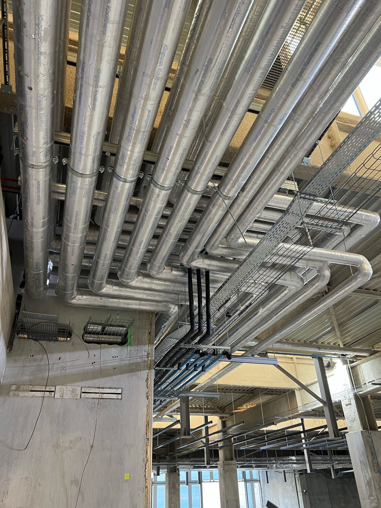 Vue aérienne du plafond inachevé d'un bâtiment avec de nombreux tuyaux et conduits disposés en rangées.