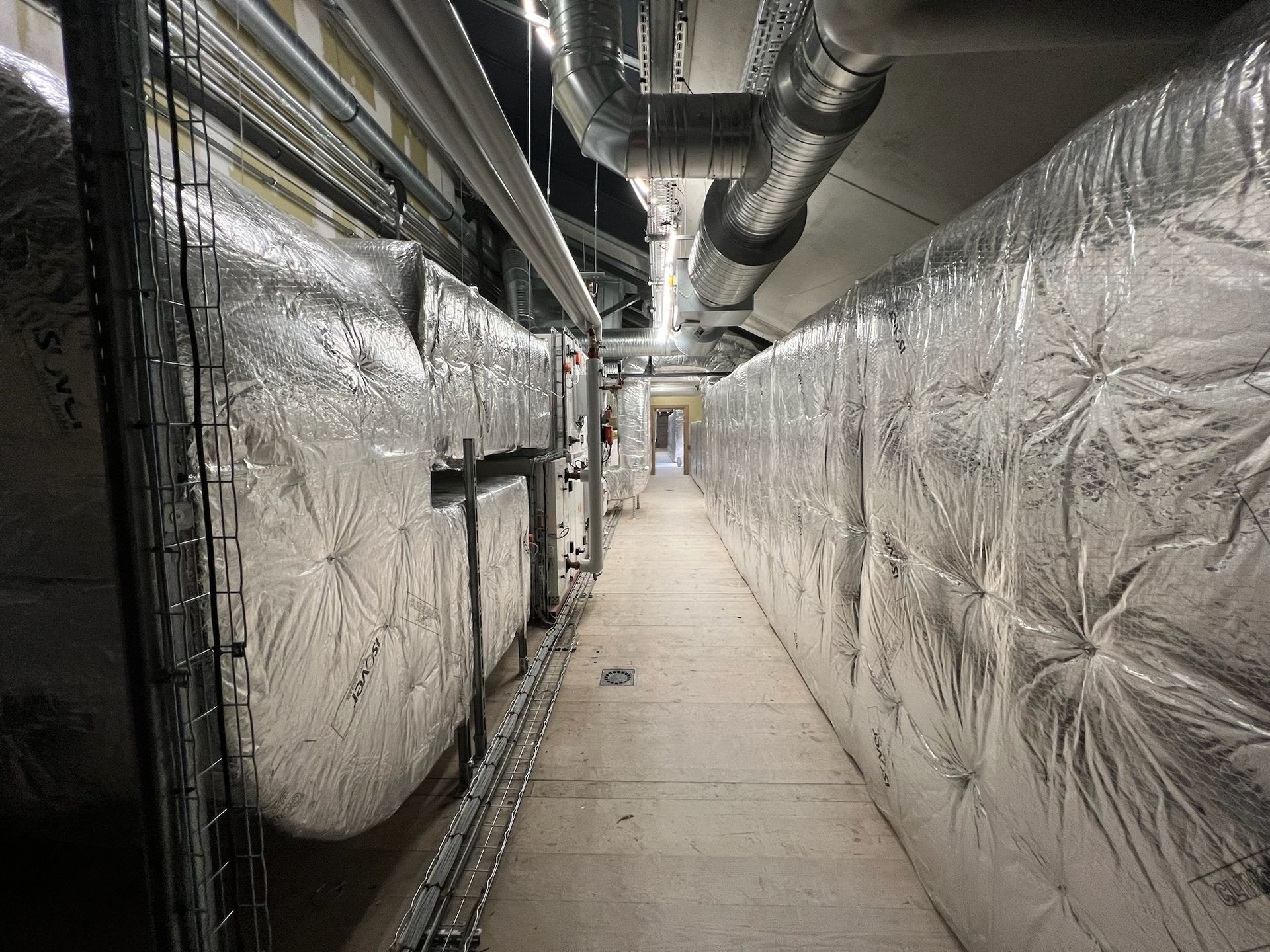 Couloir étroit avec conduits et tuyaux isolés. Sol en béton.