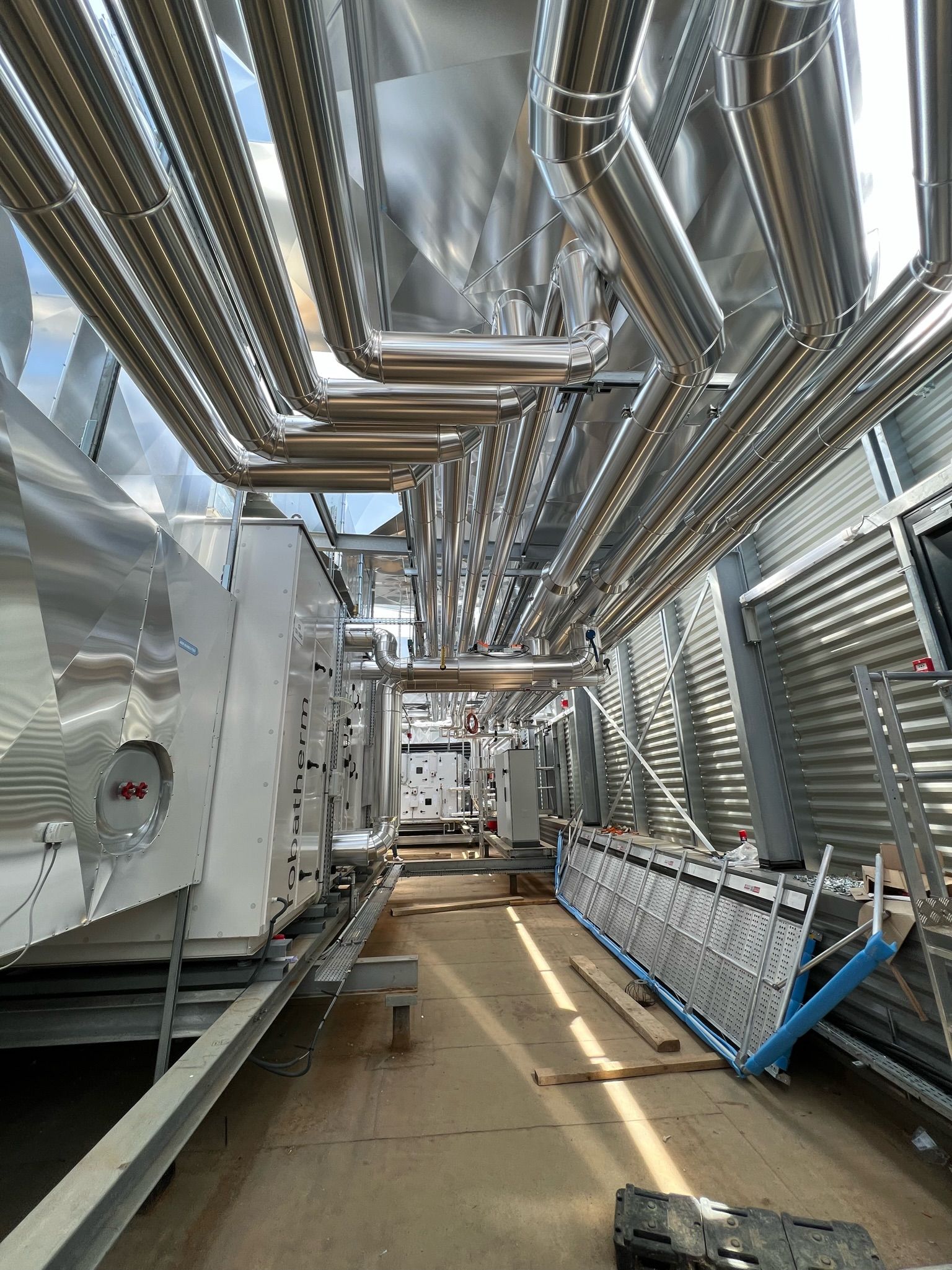 Vue intérieure du système CVC d'un bâtiment avec des tuyaux métalliques et des conduits en hauteur.