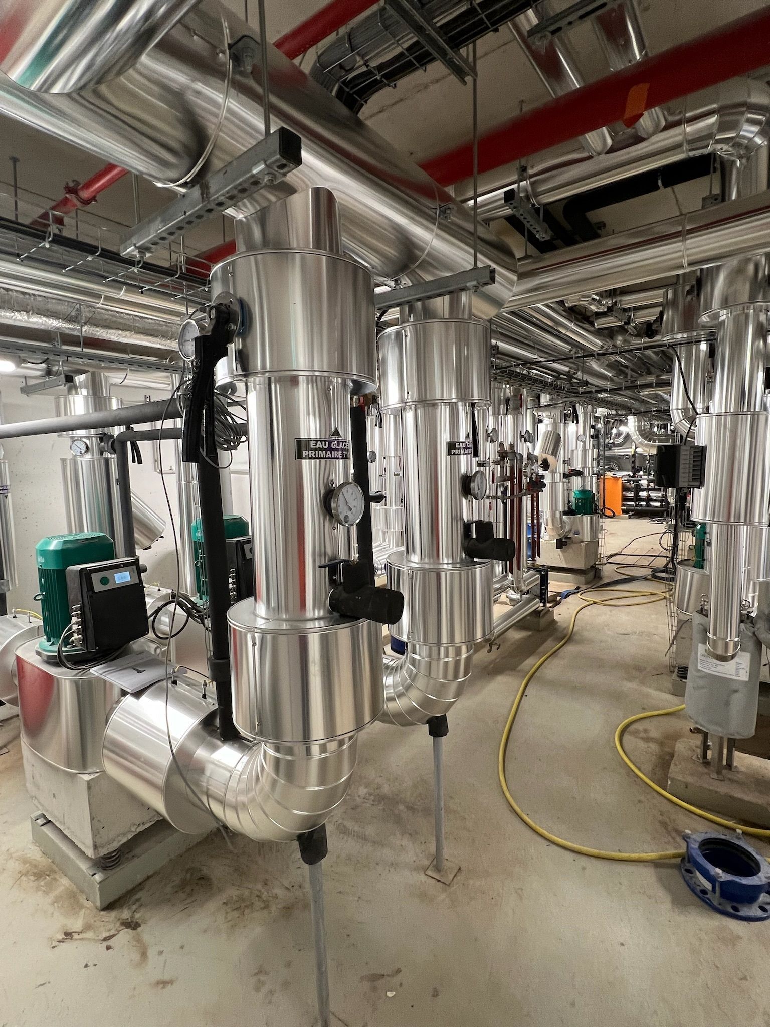 Tuyauterie et équipement industriel dans une salle mécanique, avec métal argenté et gris et jauges visibles.