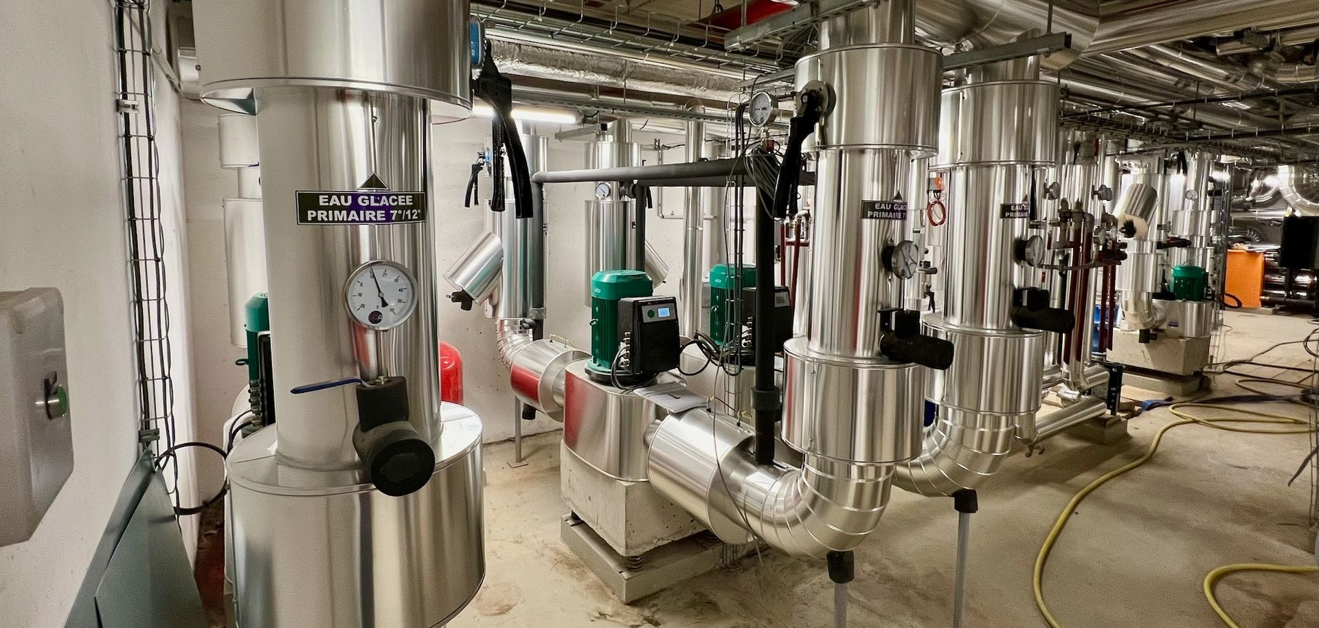 Équipement industriel, comprenant des tuyaux isolés, des jauges et des pompes dans une salle mécanique.