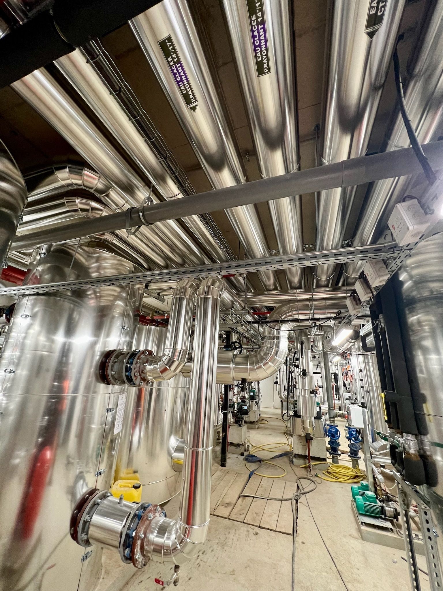Intérieur d'une installation industrielle avec tuyaux, réservoirs et équipements argentés ; éclairage lumineux.