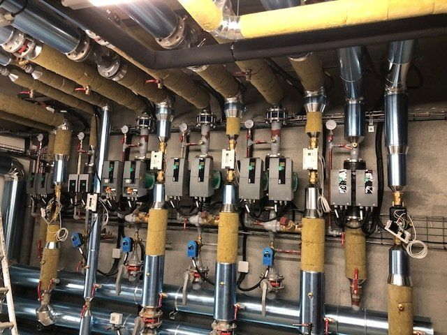 Tuyaux, vannes et pompes dans une salle mécanique, avec des sections isolées en jaune et argent.