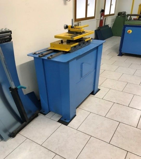 Plieuse de métal bleu, pièces jaunes, sur une table bleue dans un atelier.