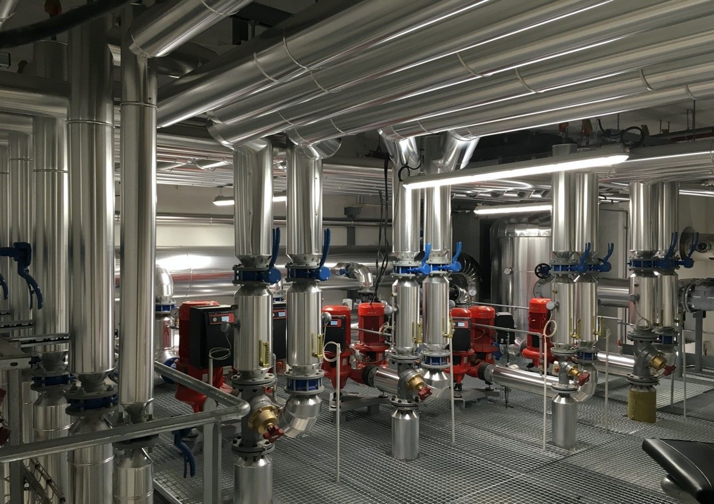 Tuyauteries industrielles avec vannes et pompes dans une salle technique. Couleurs argent, rouge et bleu.