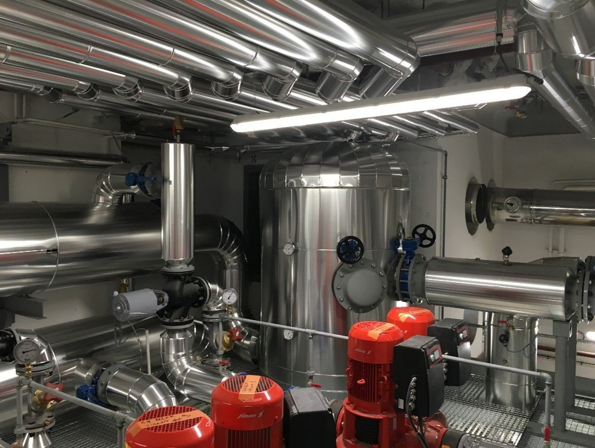 Local industriel avec tuyaux, pompes et réservoir cylindrique, le tout en métal.