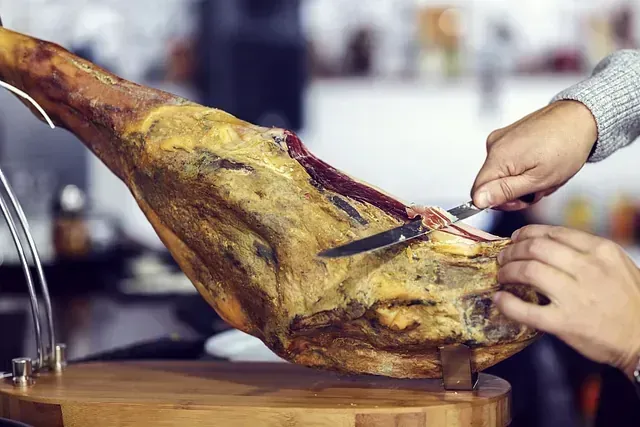 Una persona está cortando un trozo de jamón en una tabla de cortar.