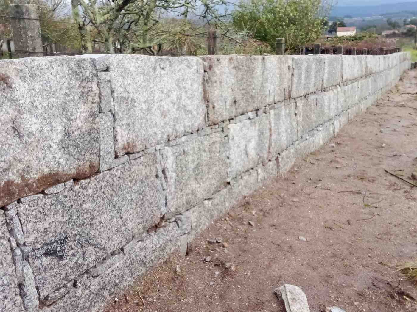 Muro de piedra a lo largo de un camino de tierra en un entorno al aire libre.
