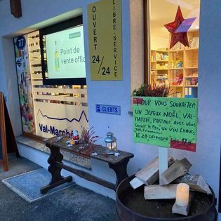 Façade de magasin avec enseignes colorées, banc et panneau « service 24h/24 » à l'entrée.