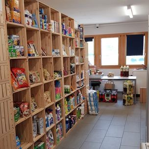 Petite épicerie avec des étagères en bois remplies de produits emballés et un comptoir vitré au fond.
