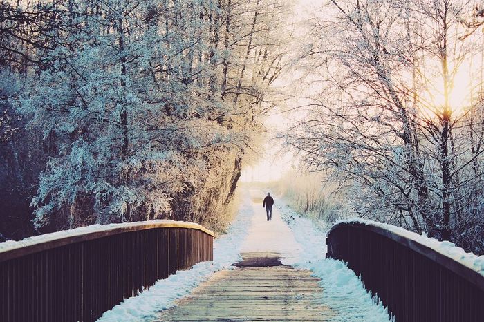 ein Mann geht auf einer schneebedeckten Holzbrücke