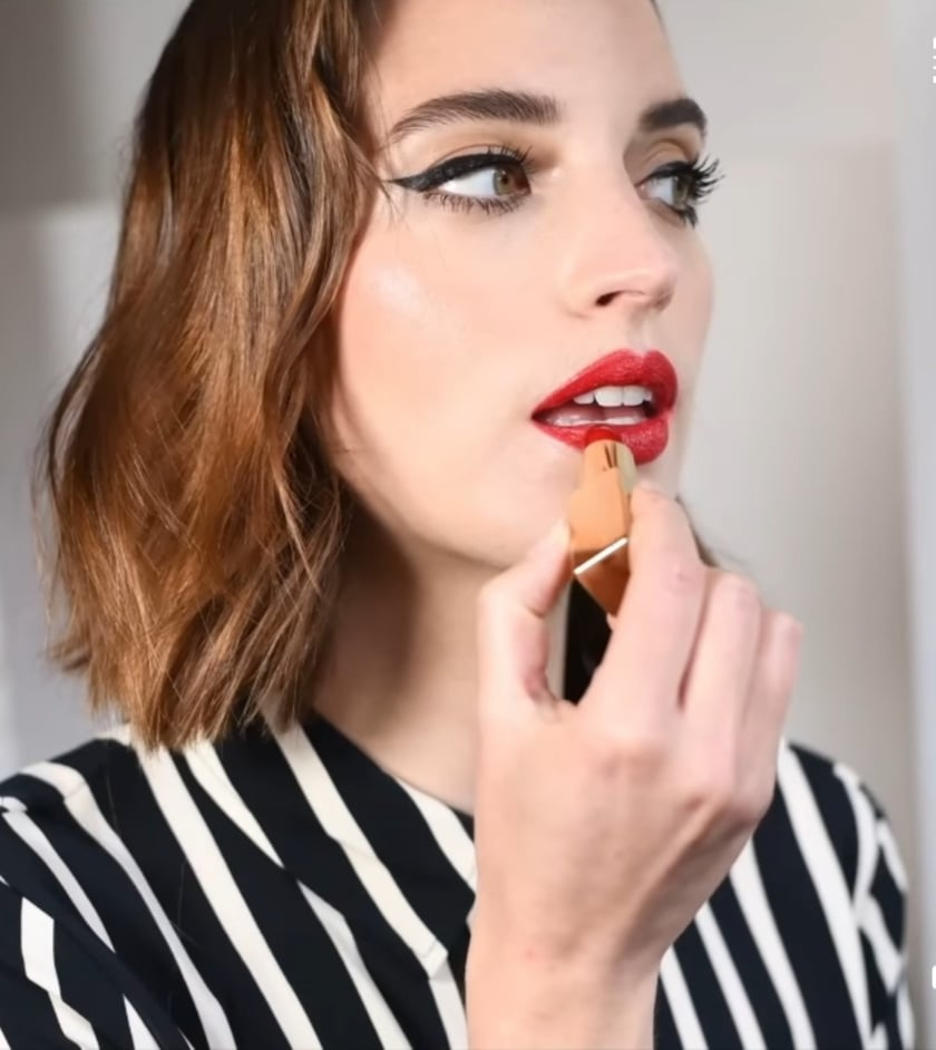 Femme portant une chemise à rayures noires, appliquant du rouge à lèvres