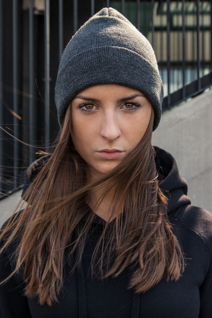 Harmaa pipo ja musta huppari yllään oleva nainen katsoo intensiivisesti ulkona olevaan kameraan.