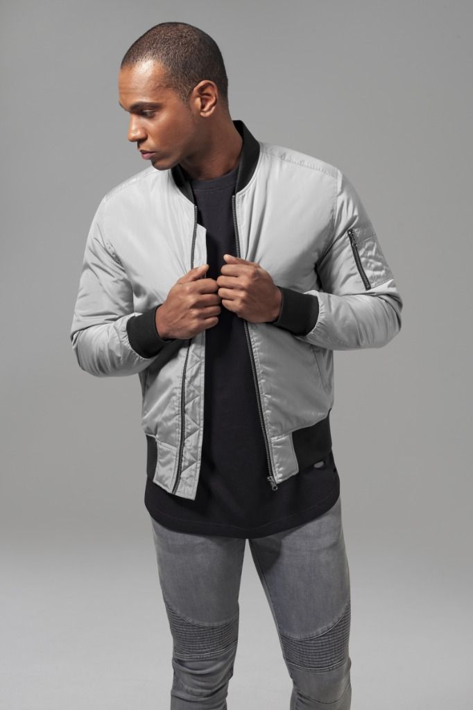 Mies harmaassa bombertakissa, mustassa paidassa ja harmaissa farkuissa pitää takkia kiinni.