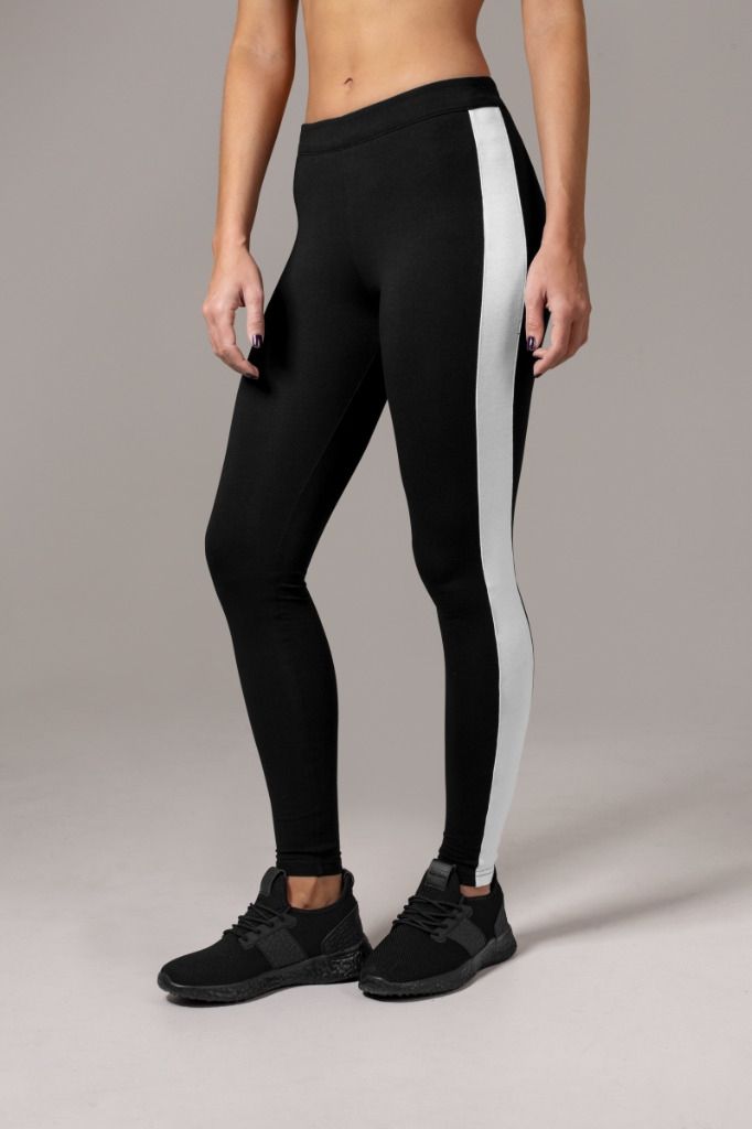 Nainen mustissa leggingsissä, joissa on valkoinen sivuraita, ja mustissa lenkkareissa.