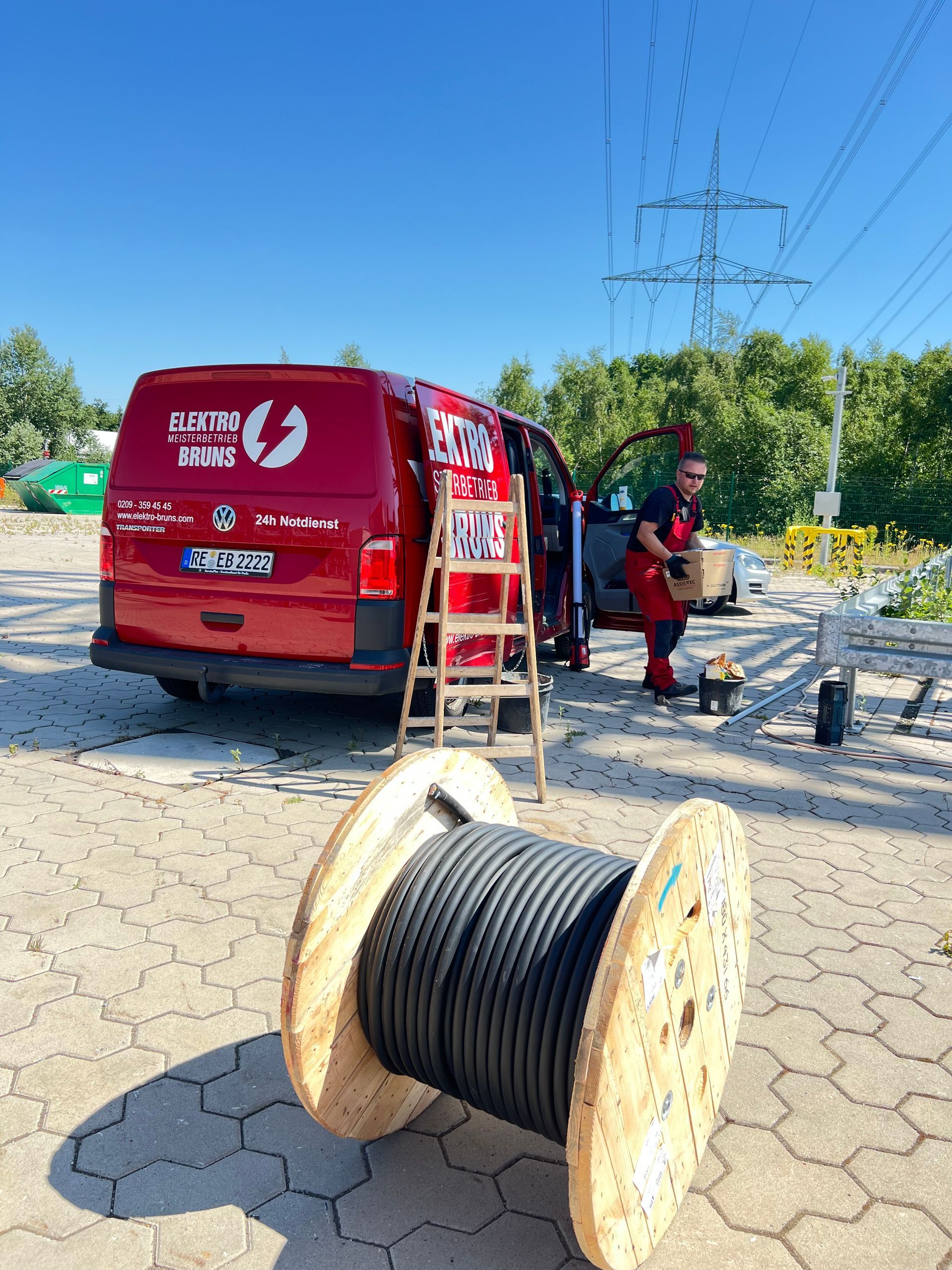 Arbeiter von Versorgungsunternehmen neben einem roten Lieferwagen und einer Kabeltrommel am Straßenrand bei klarem Himmel