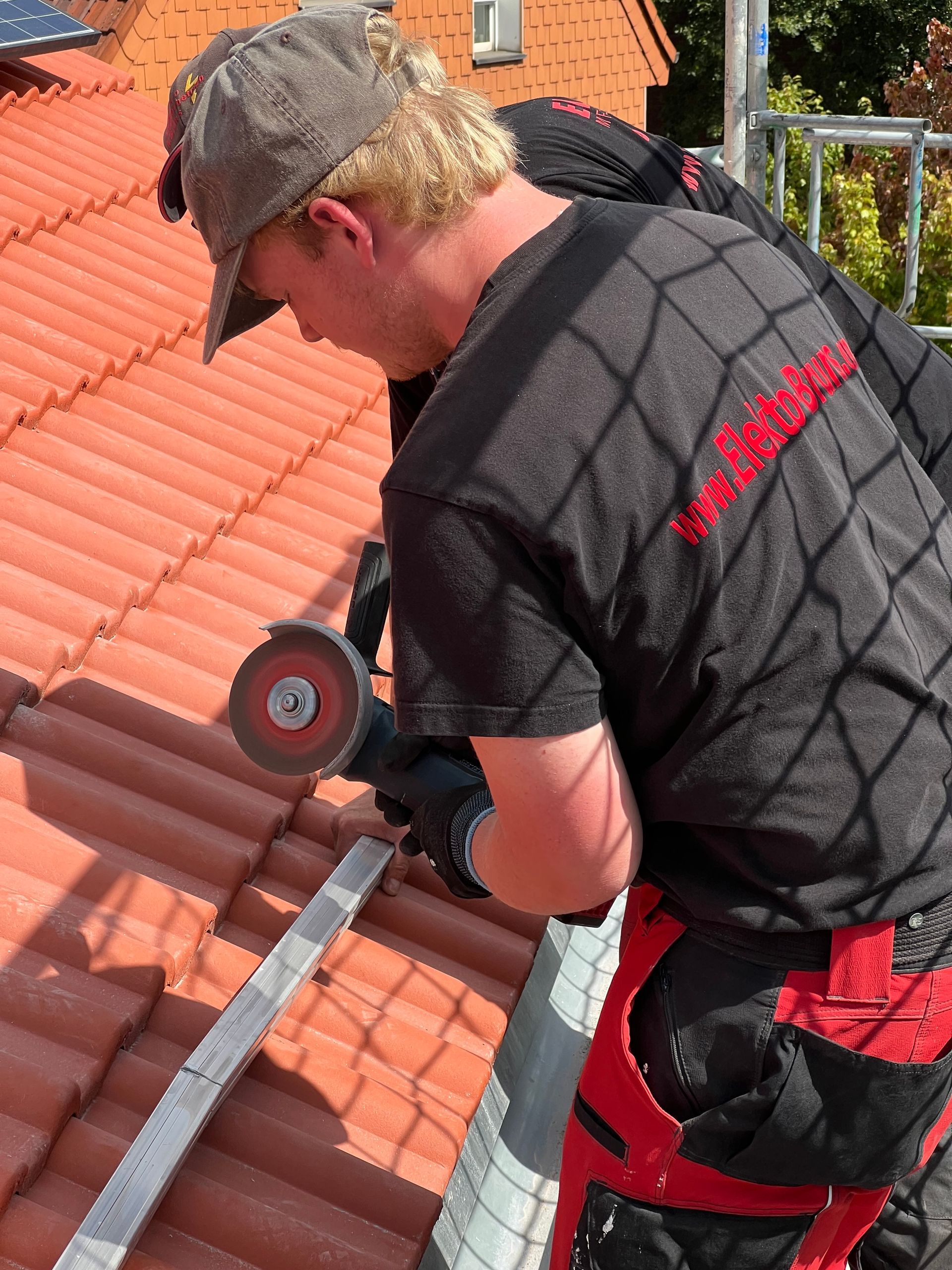 Arbeiter benutzt ein Schneidwerkzeug an roten Dachziegeln während einer Dachreparatur